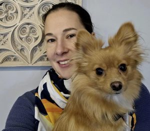 A light skinned woman with dark hair has a long haired pomeranian dog.