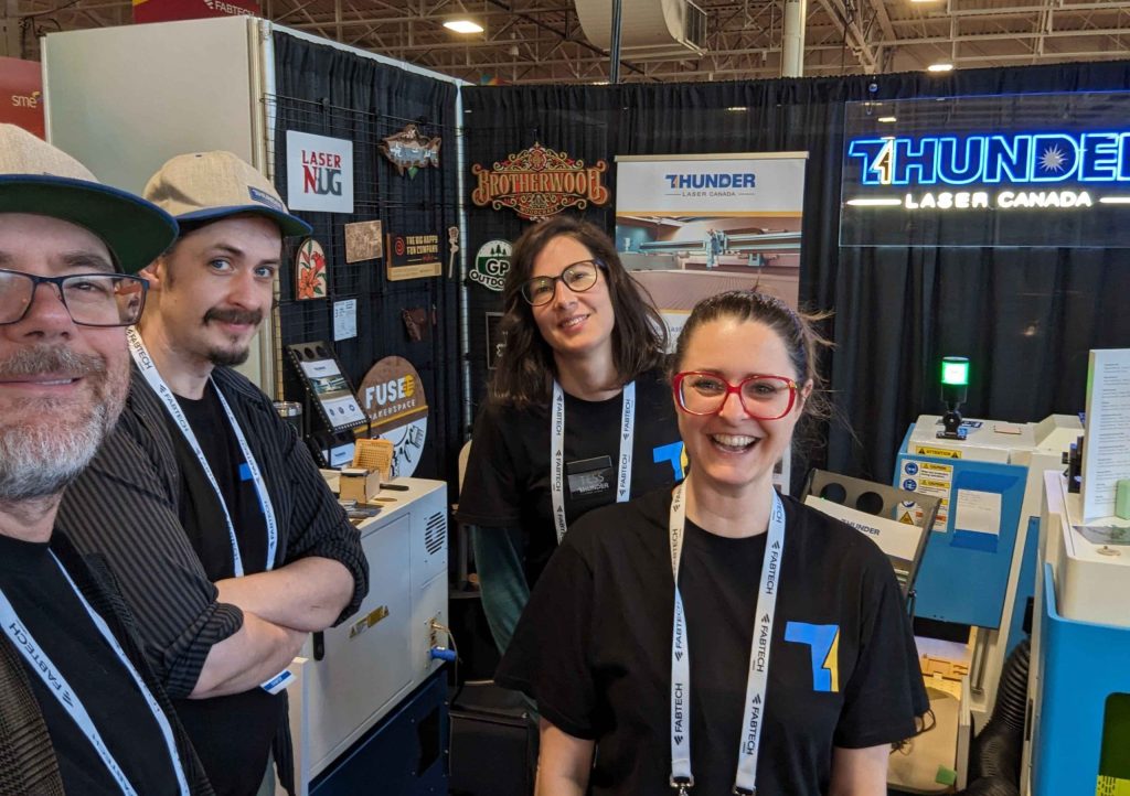 laser cutter canada Thunder Laser Canada team- 4 people standing at a trade show booth with Thunder laser machines in the background